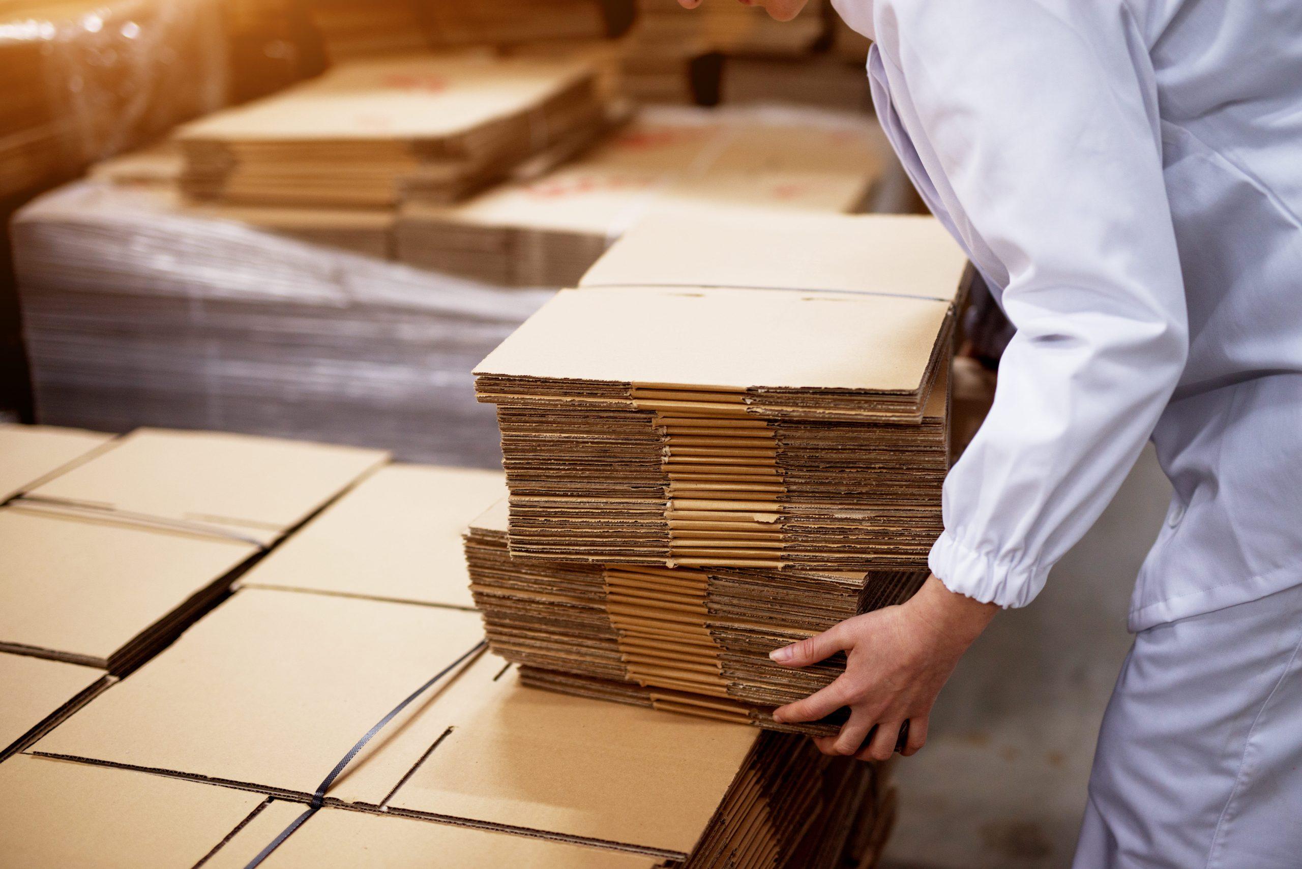 close-up-young-female-worker-picking-up-stacks-folded-cardboard-boxes-from-bigger-stack-factory-storage-room